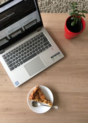 Flat lay of laptop, plant and piece of tart